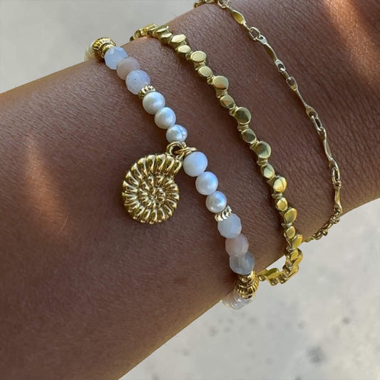 Goldener Armreif Nerea am Handgelenk getragen, kombiniert mit Armkette Nerea und weiteren Armbändern im Stapel-Look.