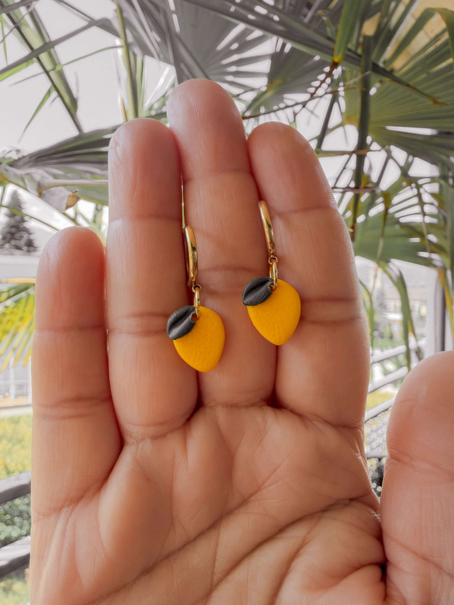 Sommerliche Zitronen Ohrringe handgemacht aus Polymer Clay an vergoldeter Creole in der Hand gehalten.