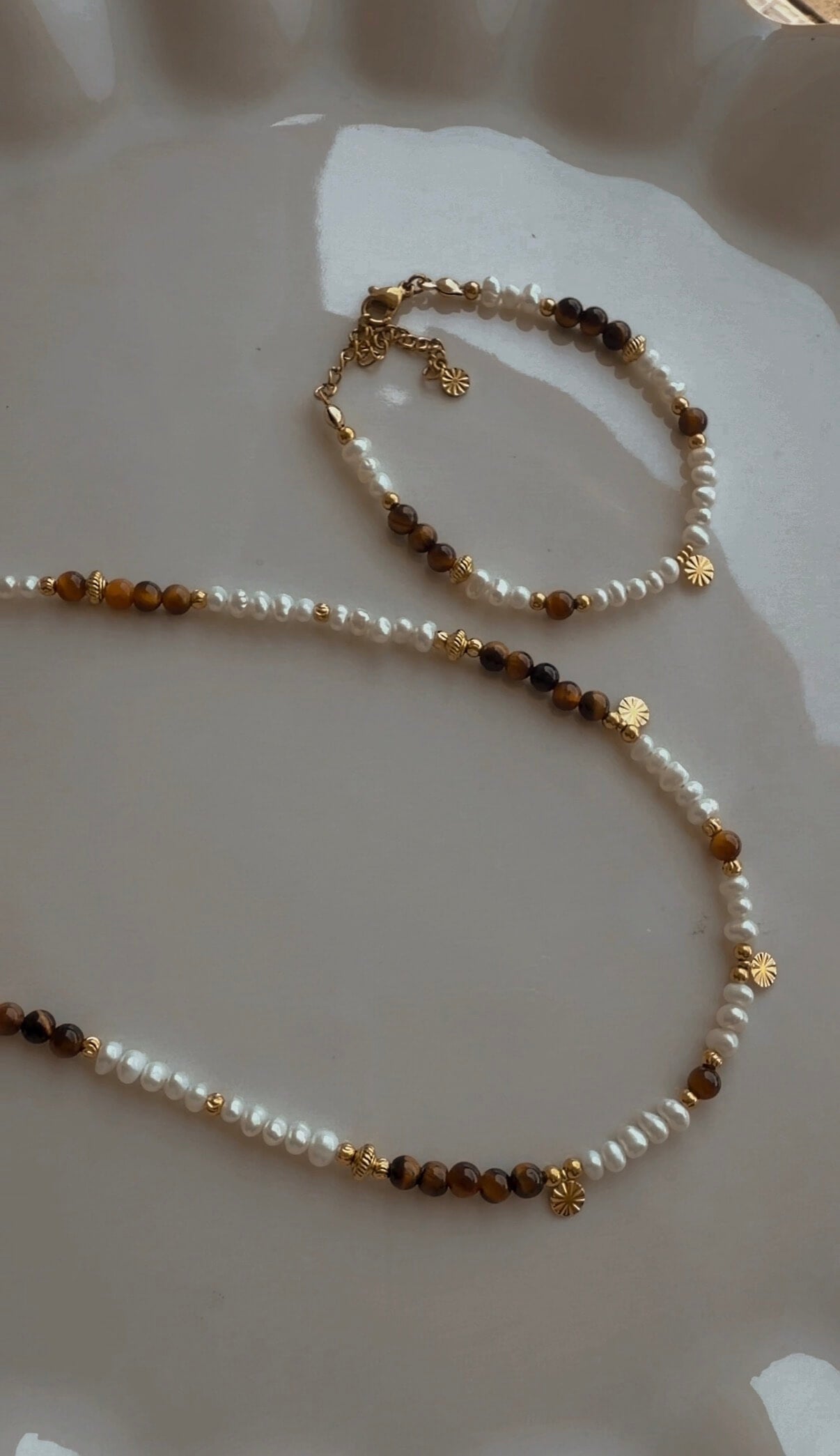 Handgefertigte Halskette und Armband aus Süsswasserperlen und Tigerauge mit vergoldeten Edelstahldetails auf Glasschale.