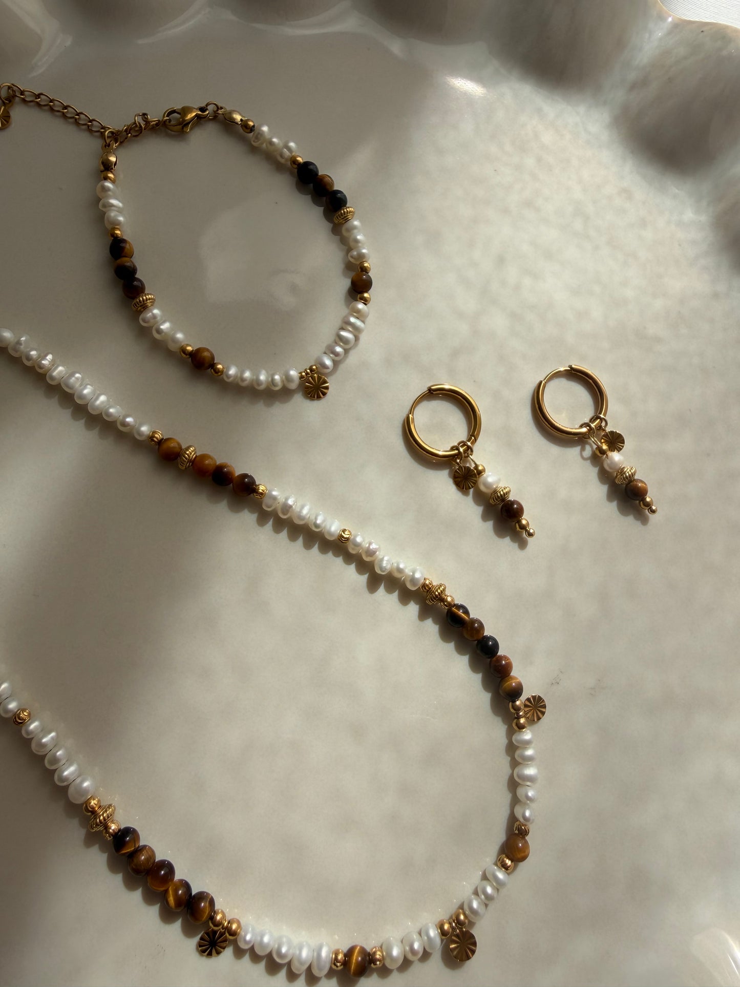 Elegante Ohrringe Solea aus 18k vergoldetem Eldestahl mit echter Süsswasserperle und Tigerauge im warmen Sonnenlicht fotografiert.