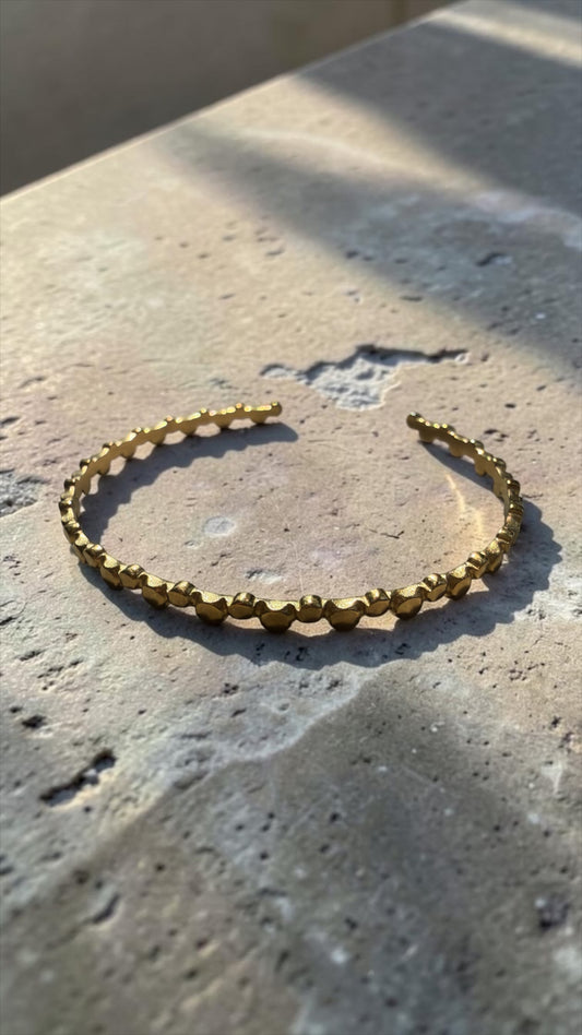 Goldener Armreif Nerea mit strukturierter Optik auf  Steinplatte.