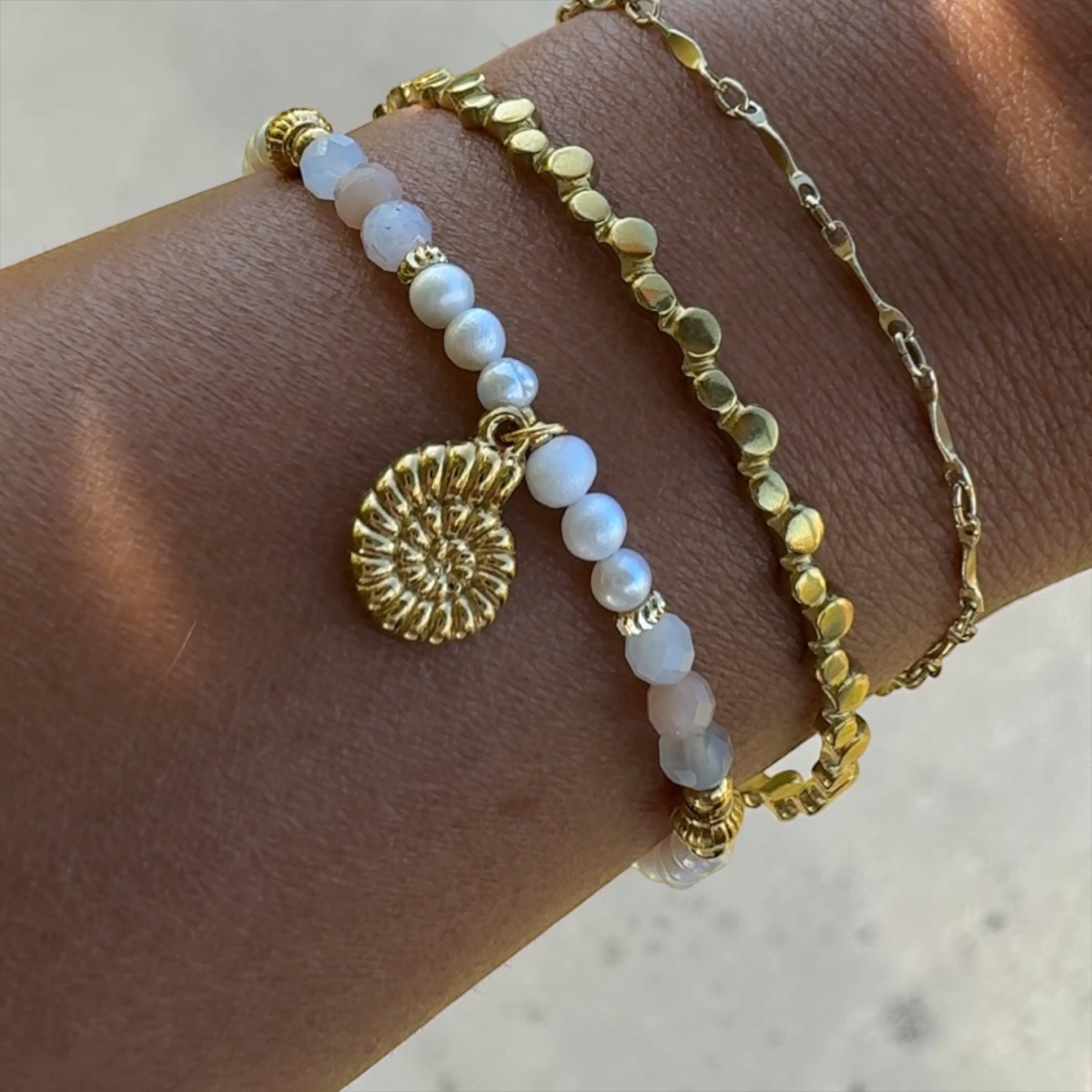 Goldener Armreif Nerea am Handgelenk getragen, kombiniert mit Armkette Nerea und weiteren Armbändern im Stapel-Look.